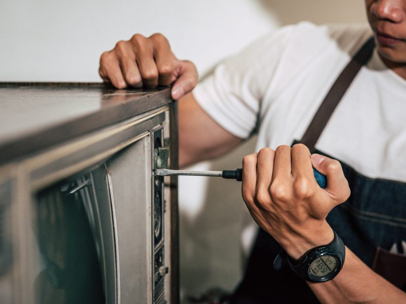 The mechanic uses a screwdriver to tighten the screws on the TV. Selective focus.